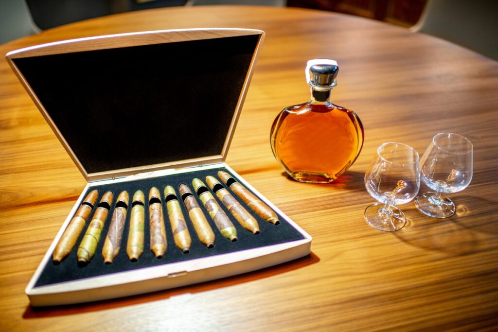 A bottle of whisky and a set of glasses on a table, perfect for enjoying aged cigars.