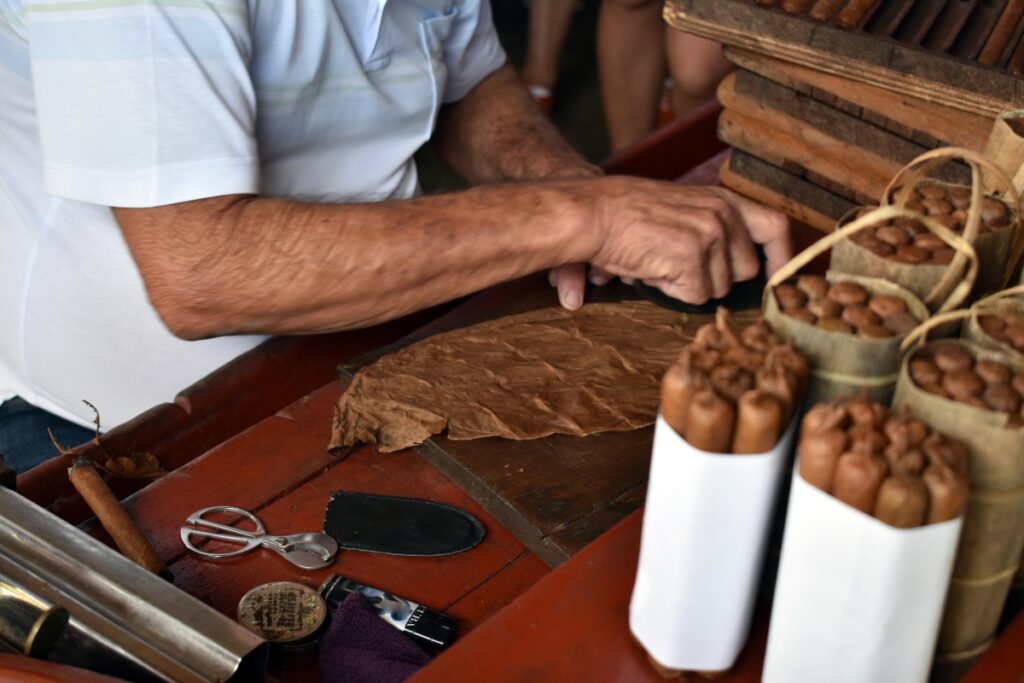 A man is cutting cigars on a wooden table as he diligently works with tobacco harvested from the fields.