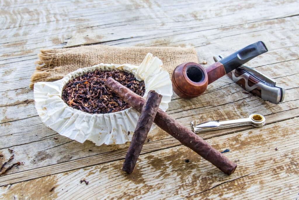 Pipes and cigars, along with pipe tobacco, are displayed on a wooden table.