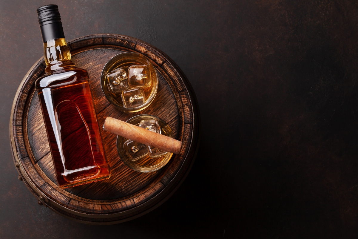 A bottle of alcohol and glasses on a barrel, perfect for cigar drink pairings.