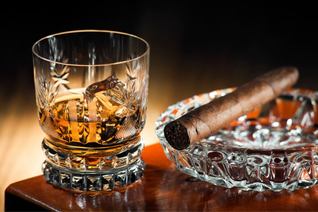 A glass of whiskey and a cigar in an ashtray, showcasing classic drink pairings.