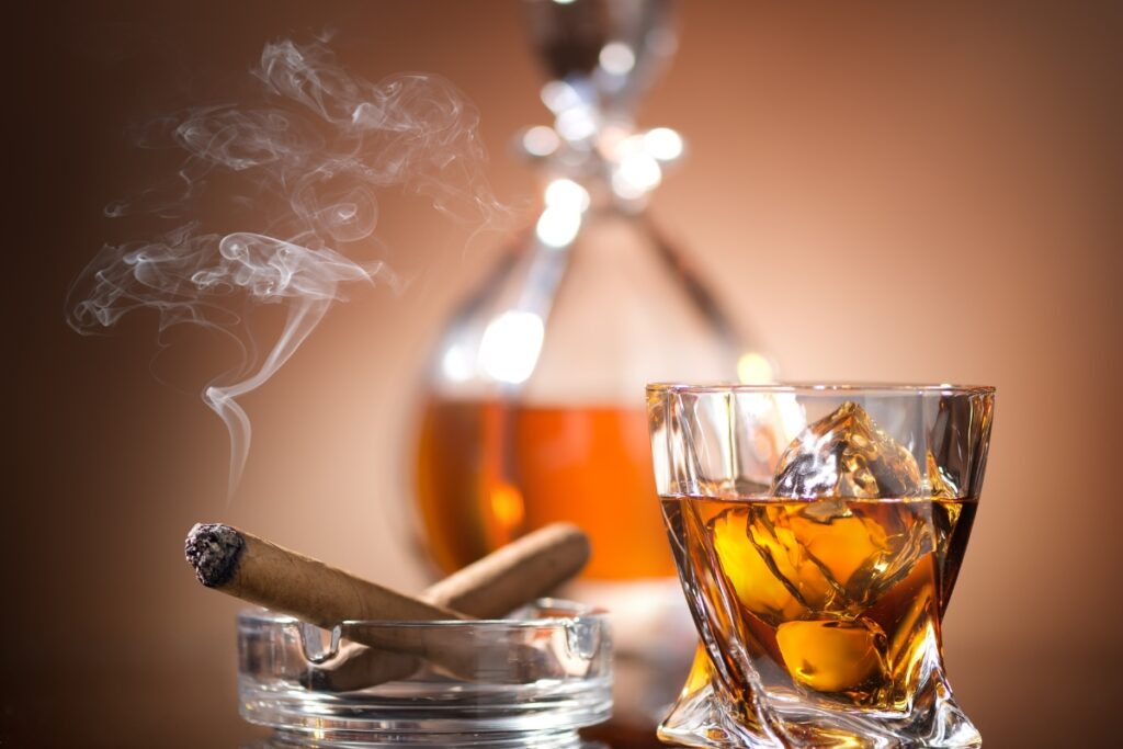 A glass of alcohol with ice and a cigar in an ashtray, exemplifying perfect cigar drink pairings.