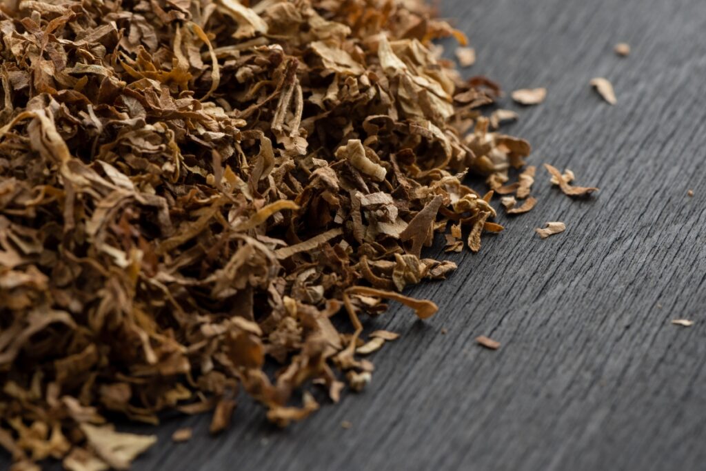 Dried, shredded brown tobacco leaves spread out on a dark, textured surface, echoing the rich Native American tobacco history.