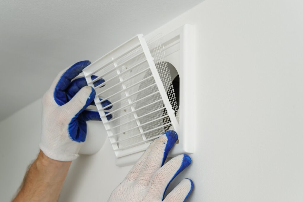 A person wearing white gloves with blue accents is installing or adjusting a white vent cover on a white wall in a home smoking lounge.