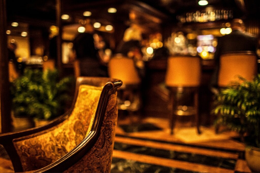 A cushioned chair in focus in a dimly lit bar, evoking the ambiance of a home smoking lounge, with patrons and barstools blurred in the background.