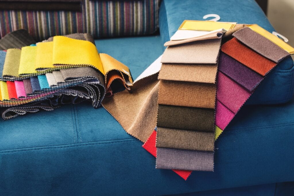 A variety of colorful fabric swatches are displayed on a blue sofa in the home smoking lounge, with each swatch labeled and arranged in an overlapping manner.