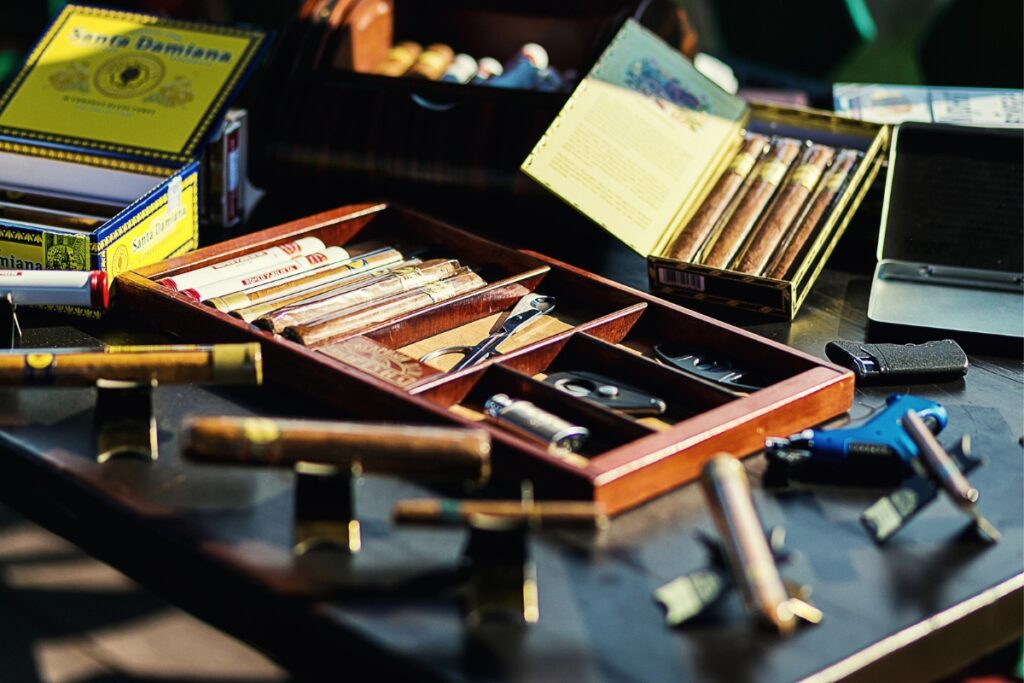 A collection of cigars in wooden trays and boxes on a table, with various accessories including cutters and a lighter, perfect for your home smoking lounge.