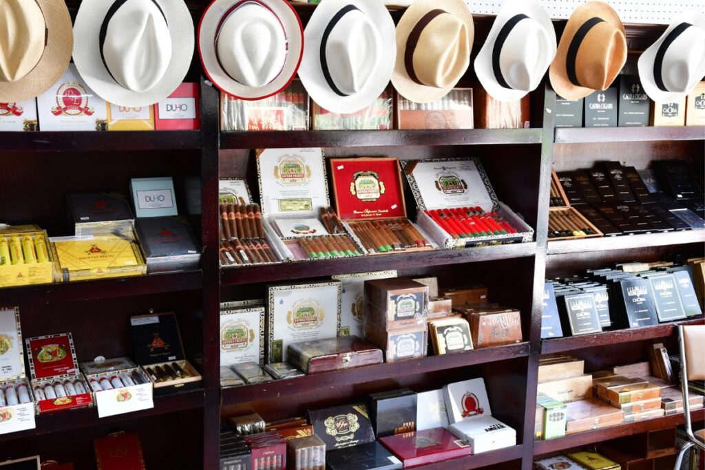 Display shelves featuring a variety of luxury cigars and cigar boxes, with a selection of hats placed on top.