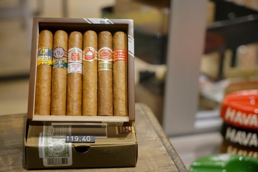 A box with six luxury cigars is displayed on a table. The price label shows 119.40. Various cigar bands are visible on the cigars.