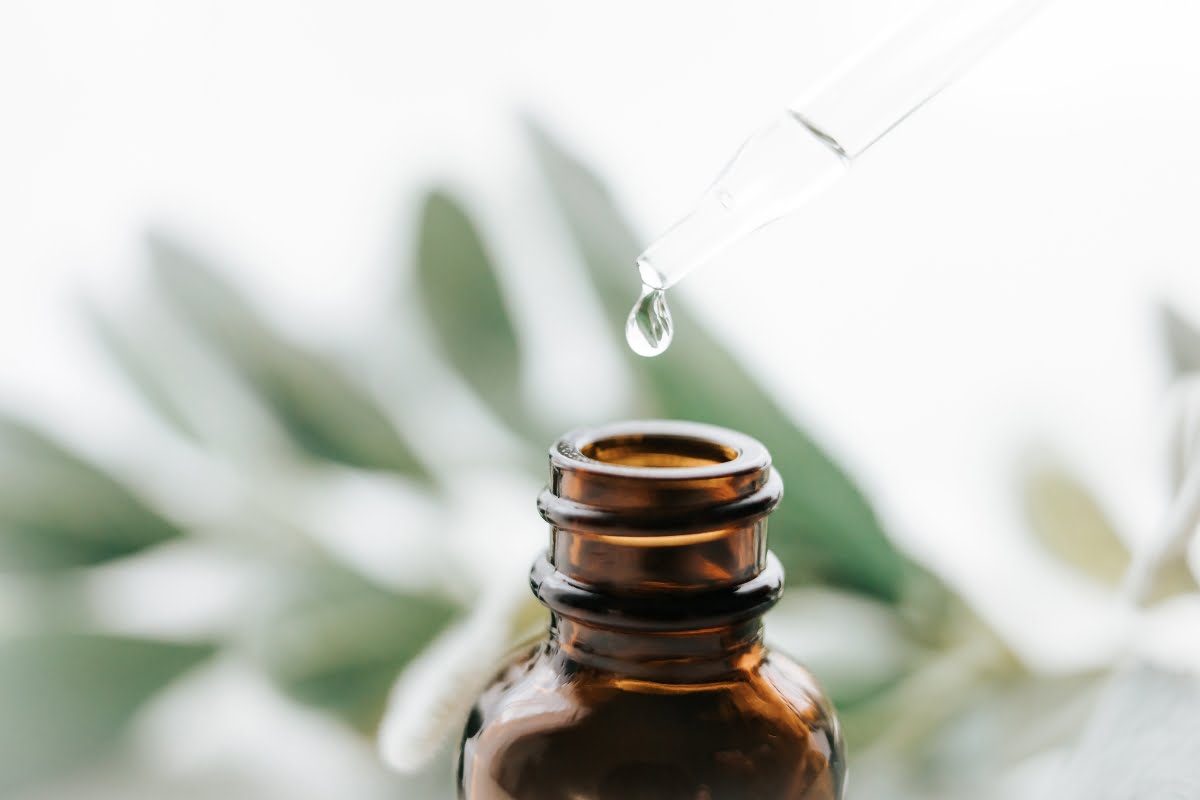 A dropper releasing a liquid drop of essential oil for smokers into a small amber glass bottle, with a blurred background of green leaves.