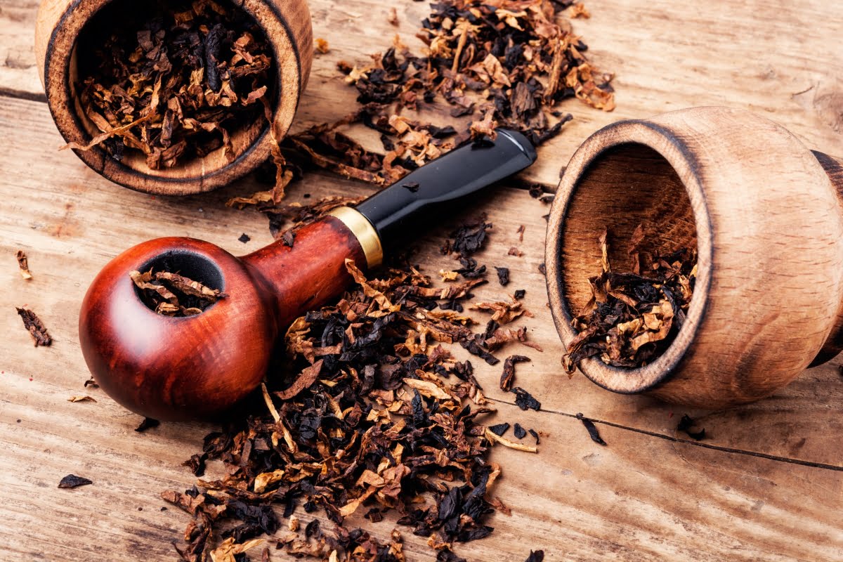 A wooden tobacco pipe lies on a table with scattered loose tobacco and two wooden bowls, one of which is overturned, showcasing classic smoking memorabilia.