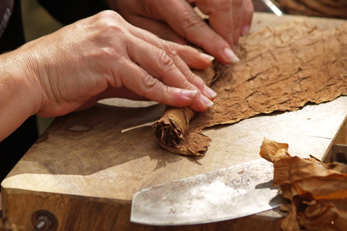 Hands skillfully rolling a cigar on a wooden surface with a knife nearby, evoking the artisanal charm one might find strolling through Marietta Square.