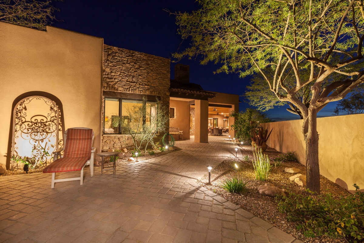 A well-lit desert-style courtyard with a stone facade, potted plants, and outdoor seating. An inviting lighted pathway leads to an open patio area, seamlessly transforming into an outdoor smoking lounge for those who wish to unwind under the stars.